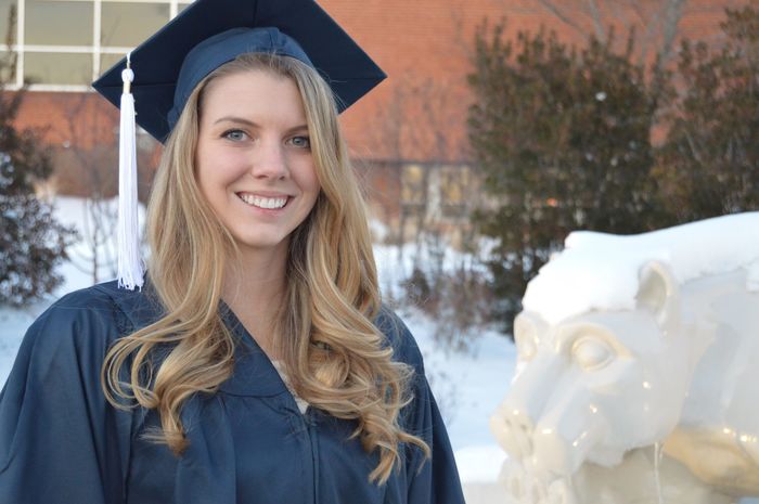 Sarah Lenhart in her cap and gown at graduation, beside the Lion