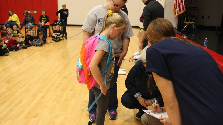 First grader Kendall Lashinsky steps on the scale in order to weigh her backpack. 