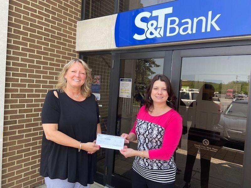 two women hold a check in front of a bank