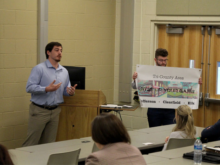 Third year student Jeff Romano gives details on his group’s marketing materials, such as the poster being displayed.