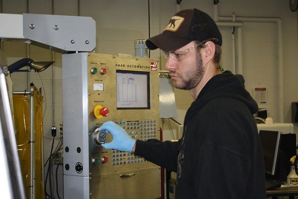 Student with black shirt and hat using a piece of equipment in the Engineering lab