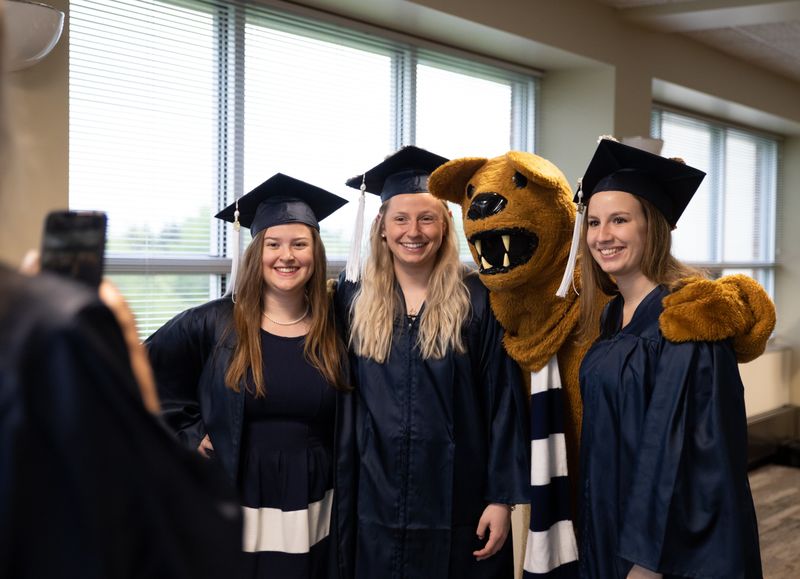 Three female graduates pose with Nittany Lion mascot Three female graduates pose with Nittany Lion mascot
