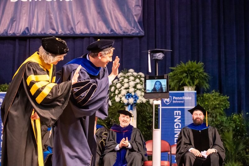 Two Penn State Behrend faculty members wave to a student whose face is on the monitor of a robot.