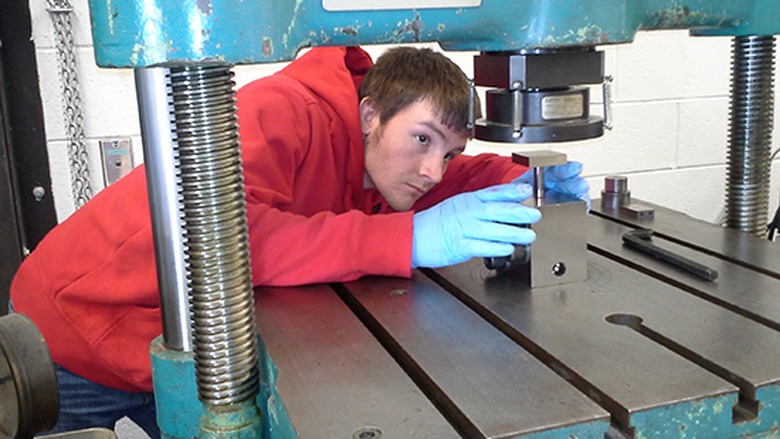 Person in a red hoodie and blue gloves works with a metal machine