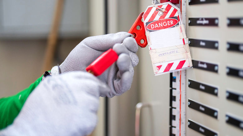 An employee, wearing proper safety protection, completes a lockout tagout procedure on a circuit breaker at the main distribution point.