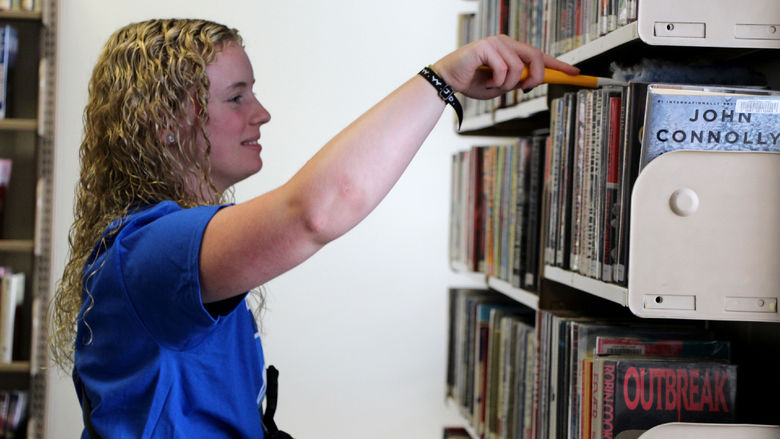 Incoming student Kamryn MacTavish dusts bookshelves at the DuBois Public Library during outreach day.