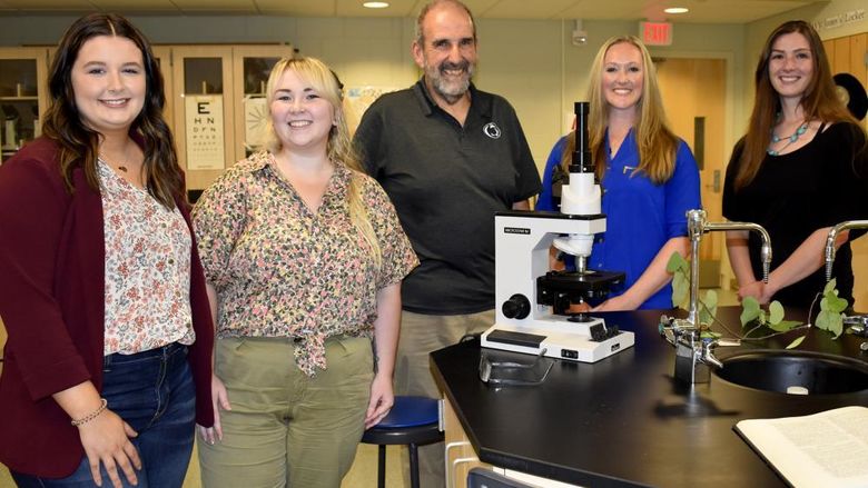 five people stand near a lab bench with a microscope on it