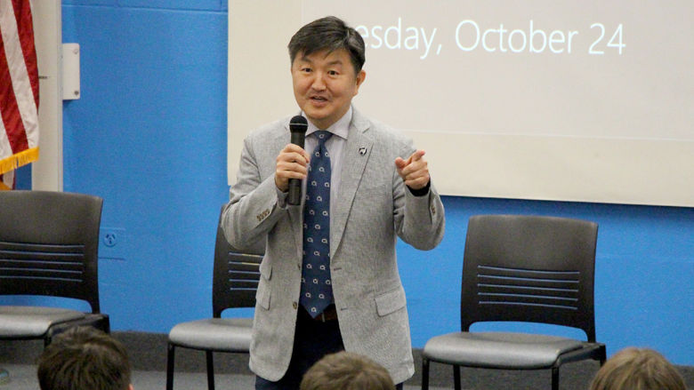 Person with a microphone stands in front of a screen. 