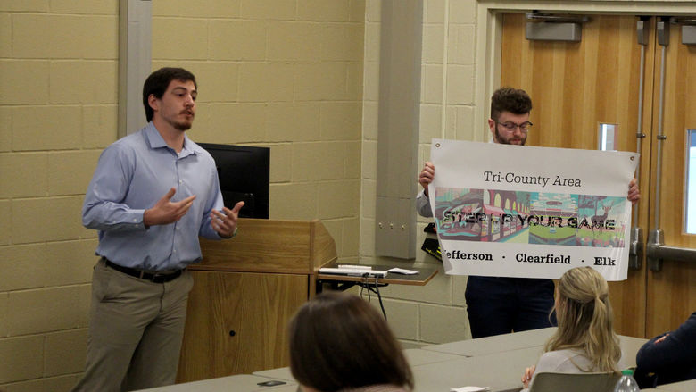 Third year student Jeff Romano gives details on his group’s marketing materials, such as the poster being displayed.