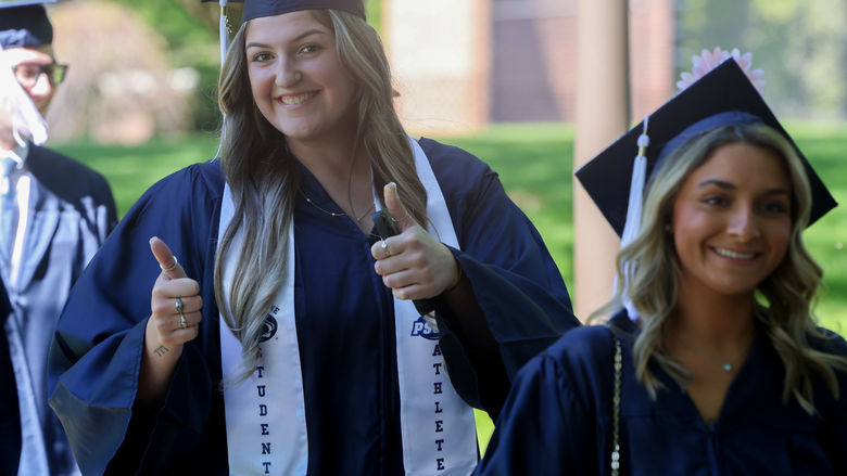 Two women are walking outside wearing commencement caps and gowns.