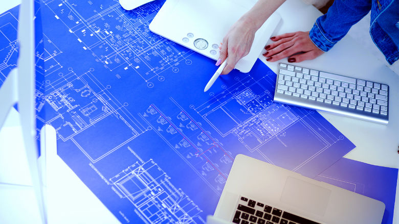 Two individuals reading and marking up a blueprint drawing
