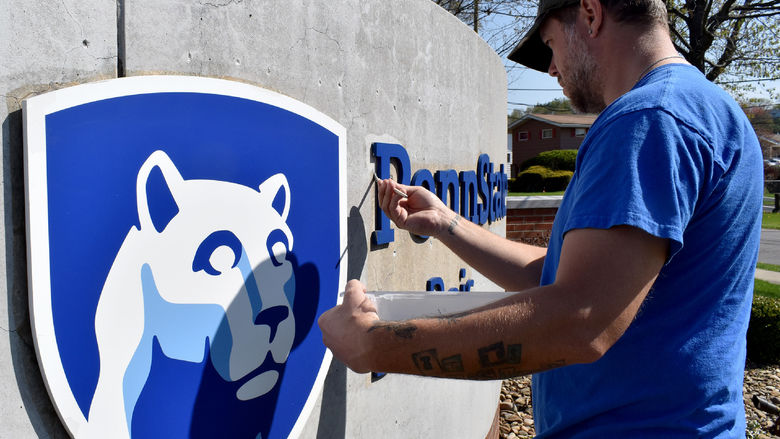 Building operations staff member Brooks Carr works through his first coat of paint during a refurbishment project on the entrance sign at Penn State DuBois.