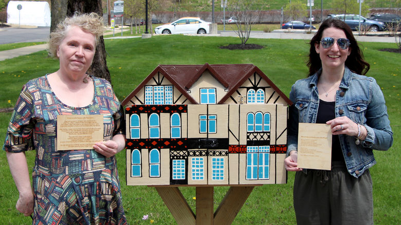 Jackie Atkins, assistant teaching professor of English, left, and Jessica Clontz, assistant teaching professor of human development and family studies, right, hold engraved plaques next to the Little Free Library that was installed and dedicated to the late Tony Vallone during a ceremony at Penn State DuBois on April 29.