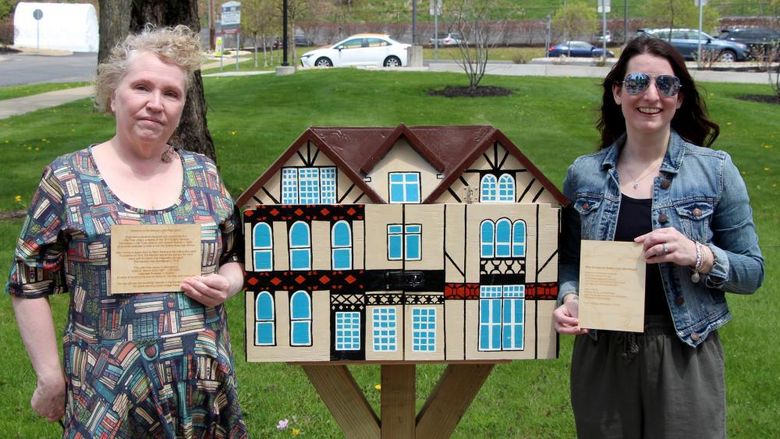 Jackie Atkins, assistant teaching professor of English, left, and Jessica Clontz, assistant teaching professor of human development and family studies, right, hold engraved plaques next to the Little Free Library that was installed and dedicated to the late Tony Vallone during a ceremony at Penn State DuBois on April 29.