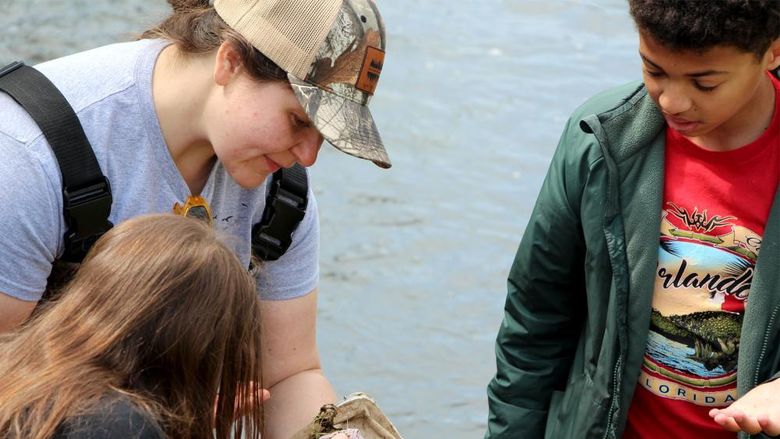 Penn State DuBois Wildlife Technology graduate Andrea Lecuyer, top left, who graduated from the program in spring 2025, works with students at Juniata Elementary in DuBois to view and study organisms found during the wetlands education program held at the school in May.
