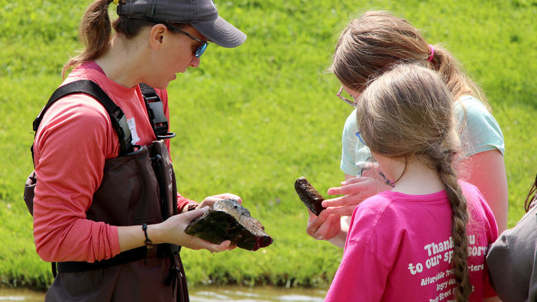 Emily Thomas, left, associate teaching professor of wildlife technology at Penn State DuBois, discusses organisms the students found on rocks within a wetlands area during the program session held at Juniata Elementary in DuBois in May.