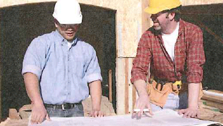 Two men with hard hats standing with blueprints on a table