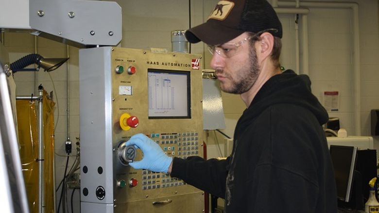Student with black shirt and hat using a piece of equipment in the Engineering lab