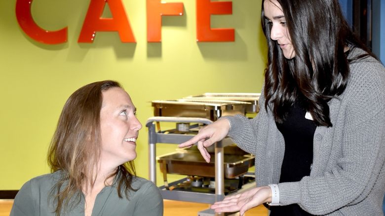 Two people talking in front of a cafe sign