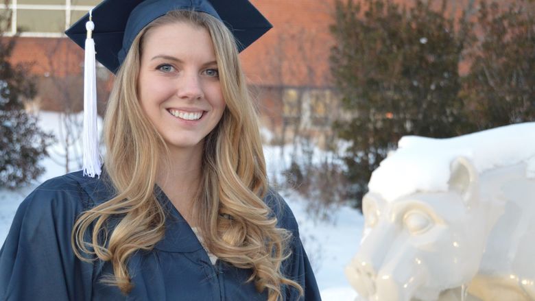 Sarah Lenhart in her cap and gown at graduation, beside the Lion