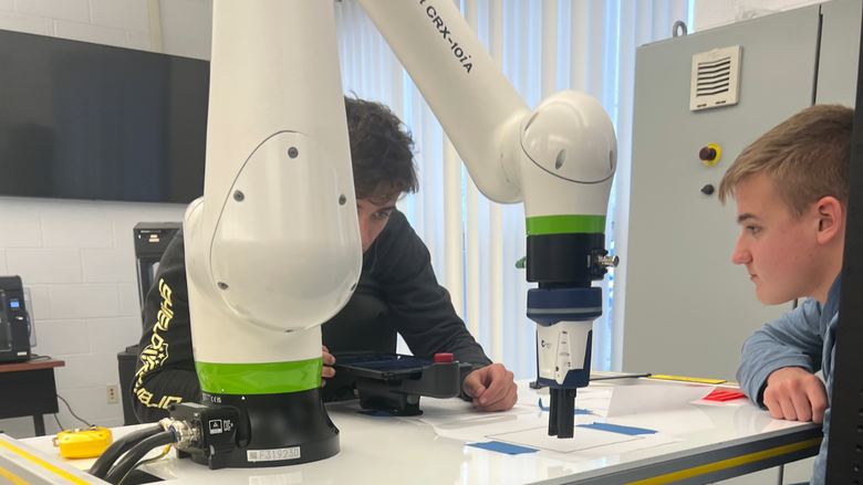 two students learning how to use a robot arm