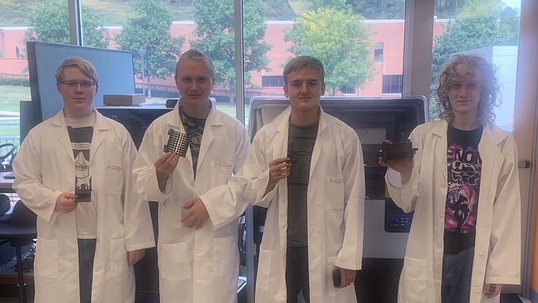 Four students in lab coats holding 3-D printed items