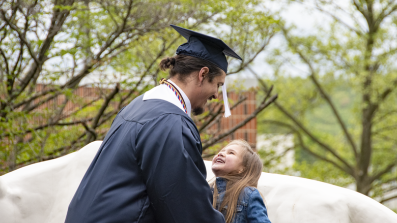 A man in academic regalia including picks up his small daughter in front of Schuylkill's lion shrine.