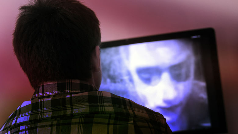 Image of the back of a viewers head while he watches a black and white zombie movie