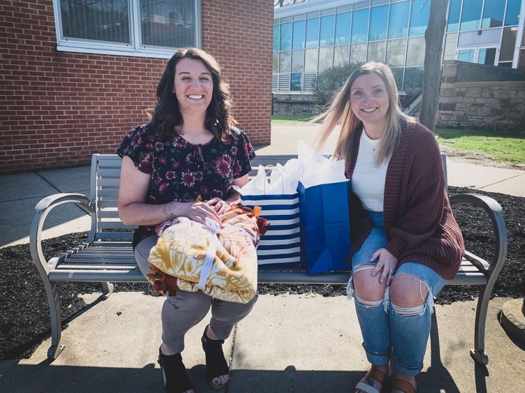 two women sit on a bench exchanging gifts