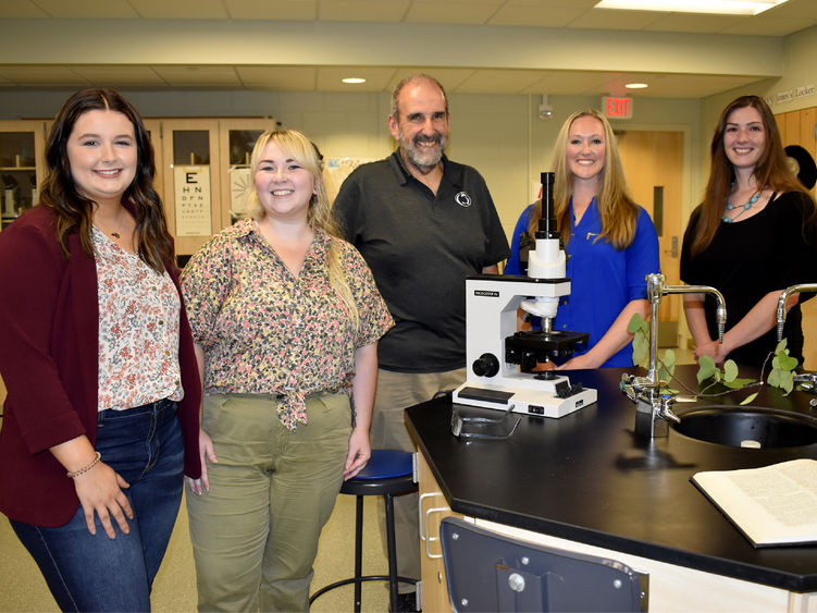 five people stand near a lab bench with a microscope on it