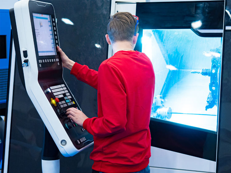 A young person watches a program run on a CNC controlled lathe.