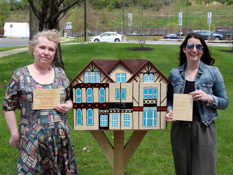 Jackie Atkins, assistant teaching professor of English, left, and Jessica Clontz, assistant teaching professor of human development and family studies, right, hold engraved plaques next to the Little Free Library that was installed and dedicated to the late Tony Vallone during a ceremony at Penn State DuBois on April 29.