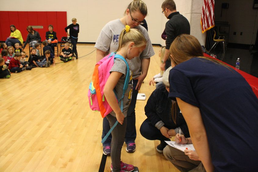 First grader Kendall Lashinsky steps on the scale in order to weigh her backpack. 