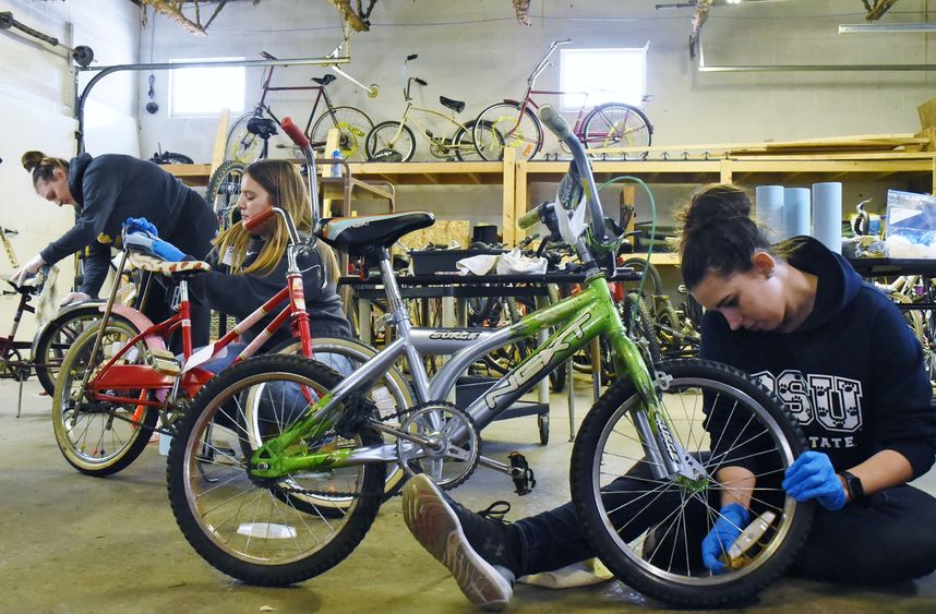 Three Penn State students repair bicycles at the Sisters of St. Joseph Neighborhood Network bike warehouse.