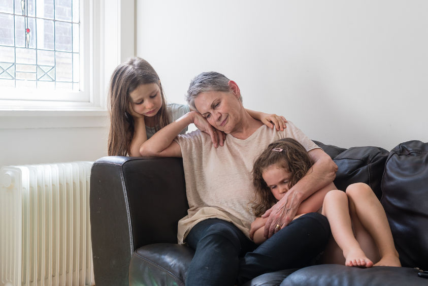 sad grandmother on couch with 2 granddaughters