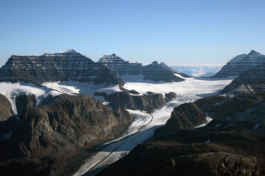 Glaciers and lava flows, east Greenland. The layered rocks in the high peaks formed when the Iceland hot spot broke through after passing beneath Greenland. The main ice sheet is visible in the distance. glaciers and lava flows, east Greenland