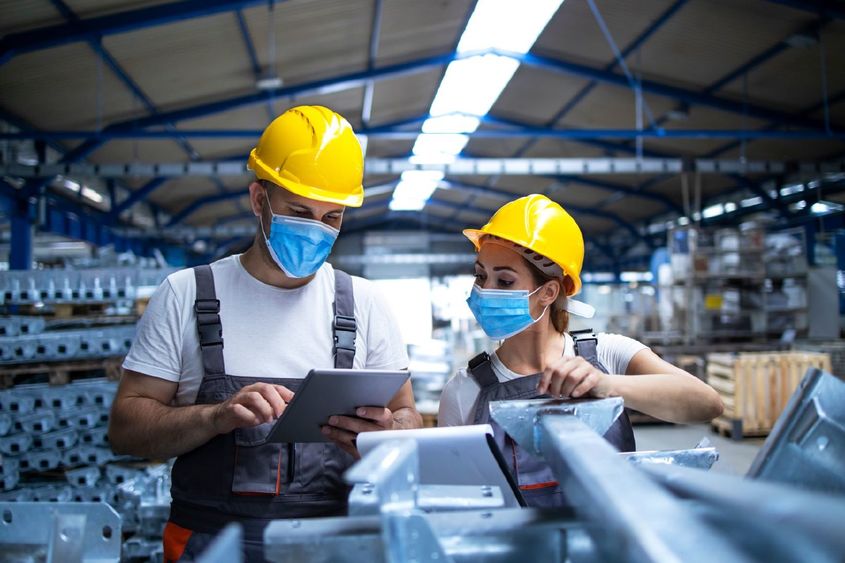 Two masked manufacturing workers in a manufacturing/factory setting