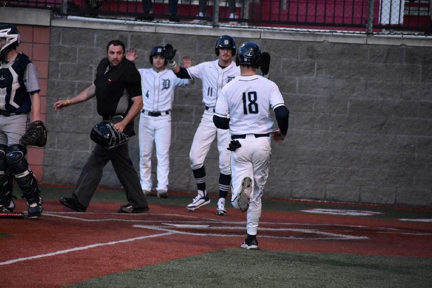 Baseball players welcome teammates at home plate after scoring